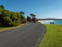 a bench sits on the edge of the empty road by the water's edge