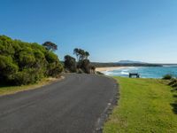 a bench sits on the edge of the empty road by the water's edge