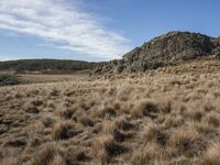 a brown grassy area with a rocky outcrop in the distance, and a hill on both sides