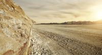 the sun sets as a lone motorcycle rides down an empty dirt road near some mountains