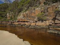 the water is clear and the rocks are brown, with a few little clouds in the sky