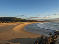 a very pretty big sandy beach next to a big hill of rocks, and a wave rolling in