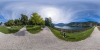 an 360 - degree image showing the same area with one bench and two trees, with a lake and mountains in the background