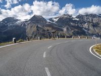 a person is riding their bicycle on a road below a mountain and snow capped peaks