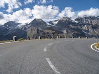 a person is riding their bicycle on a road below a mountain and snow capped peaks