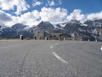 a person is riding their bicycle on a road below a mountain and snow capped peaks