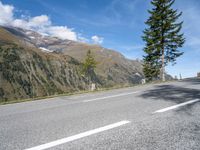 the lone white motorcycle is parked next to the road with mountains in the background and clouds on the sky