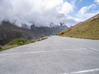 a car parked at the side of an empty road in mountains under cloudy skies and a few small clouds