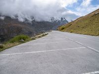 a car parked at the side of an empty road in mountains under cloudy skies and a few small clouds