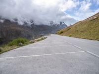 a car parked at the side of an empty road in mountains under cloudy skies and a few small clouds