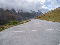 a car parked at the side of an empty road in mountains under cloudy skies and a few small clouds