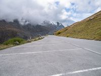 a car parked at the side of an empty road in mountains under cloudy skies and a few small clouds