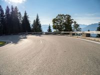 an empty asphalt road near a tree filled area and sky with clouds in the background