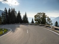 an empty asphalt road near a tree filled area and sky with clouds in the background