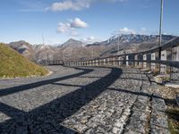 a paved road passing over a hill with snow capped mountains behind it and shadows of two people in the distance