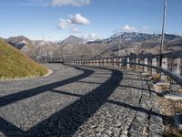 a paved road passing over a hill with snow capped mountains behind it and shadows of two people in the distance