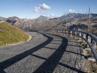 a paved road passing over a hill with snow capped mountains behind it and shadows of two people in the distance