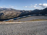 a view of the mountainous mountains and a train traveling along it, from above on a cobblestone road