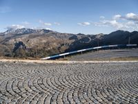 a view of the mountainous mountains and a train traveling along it, from above on a cobblestone road