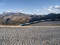 a view of the mountainous mountains and a train traveling along it, from above on a cobblestone road