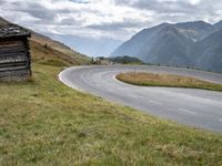 a van driving down an empty country road surrounded by mountains and grassy fields under grey skies