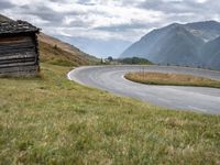 a van driving down an empty country road surrounded by mountains and grassy fields under grey skies