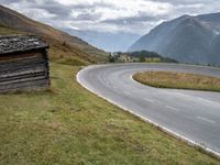 a van driving down an empty country road surrounded by mountains and grassy fields under grey skies