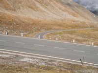 a lone skateboarder walks along an empty country road on a steep hill with mountains in the background