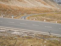 a lone skateboarder walks along an empty country road on a steep hill with mountains in the background