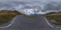 a curved curved road going past some mountains under cloudy skies overhead the image is taken at 360 angle