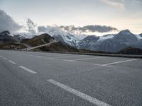 a lone road leads up to a mountain with snow covered mountains in the background and mountains