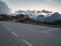 a lone road leads up to a mountain with snow covered mountains in the background and mountains