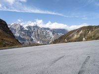 a man rides his skateboard down the paved road near snowy mountains in the distance