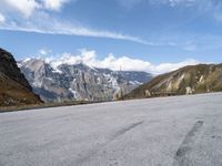 a man rides his skateboard down the paved road near snowy mountains in the distance