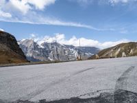 a man rides his skateboard down the paved road near snowy mountains in the distance