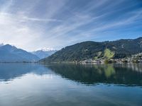 a calm lake near the mountains in the summer time in switzerland, surrounded by a town and green hills