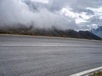 a car driving along the road in front of a large mountain and clouds on an overcast day