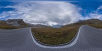 a panoramic image of two curved roads on a grassy field and mountains in the background