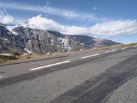 a skateboarder riding down the side of an empty road near a mountain with snow capped mountains