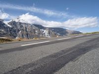 a skateboarder riding down the side of an empty road near a mountain with snow capped mountains