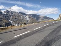 a skateboarder riding down the side of an empty road near a mountain with snow capped mountains