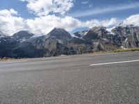 a person riding a skateboard down an empty road with snowy mountains behind him on a cloudy day