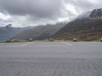 a lone skateboard parked in the middle of a road with mountains and foggy clouds