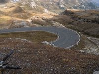 the winding road goes through the mountains into the distance, with bicycle in the foreground