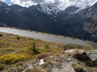 a group of motorcycles driving down the road in front of snowy mountains with a cloudy sky