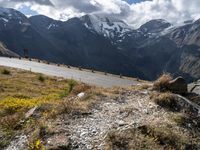 a group of motorcycles driving down the road in front of snowy mountains with a cloudy sky