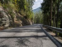 a long empty paved road on a mountain side surrounded by evergreen trees with mountains in the distance