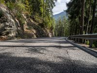 a long empty paved road on a mountain side surrounded by evergreen trees with mountains in the distance