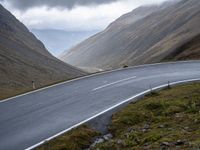 a motorcycle riding down the middle of an empty road next to mountains under a cloudy sky