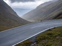 a motorcycle riding down the middle of an empty road next to mountains under a cloudy sky